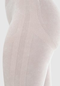 Przezroczyste cieliste rajstopy z teksturowanymi wzorami prążkowymi, gładkim wykończeniem i subtelnym połyskiem, podkreślające dopasowany i elegancki fason.