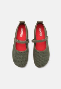 Paire de chaussures Mary Jane en mesh vert olive avec brides ajustables et semelles intérieures rouges brandées "Camper" sur fond blanc.