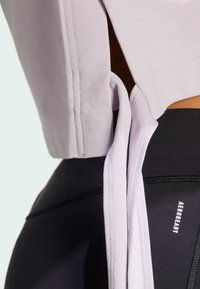 Lichtpaarse cropped top met zijknoopjes, voorzien van een zachte textuur en nette stiksels, gecombineerd met zwarte high-waisted sportleggings.