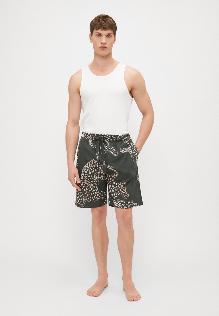 Shorts de bain verts à motif avec une taille à cordon, présentant un design de formes de léopard rose pâle et des poches latérales. Associés à un débardeur blanc.