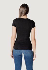 Camiseta negra de manga corta hecha de algodón suave, diseño ajustado con cuello redondo, vista desde atrás, combinada con jeans azules.