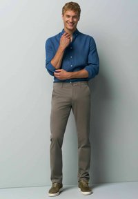 Blue button-up shirt with rolled sleeves, beige chinos, and olive sneakers; features a slim fit and a casual design.
