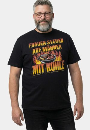 Mężczyzna w średnim wieku z okularami i brodą, ubrany w czarną koszulkę, prezentujący płonący grill oraz niemiecki tekst o kobietach, które chcą mężczyzn z węglem drzewnym.