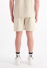 Beige katoenen shorts met een relaxte pasvorm, gecombineerd met witte sneakers en zwart-wit gestreepte sokken. Eenvoudig ontwerp, zonder zichtbare logo's.