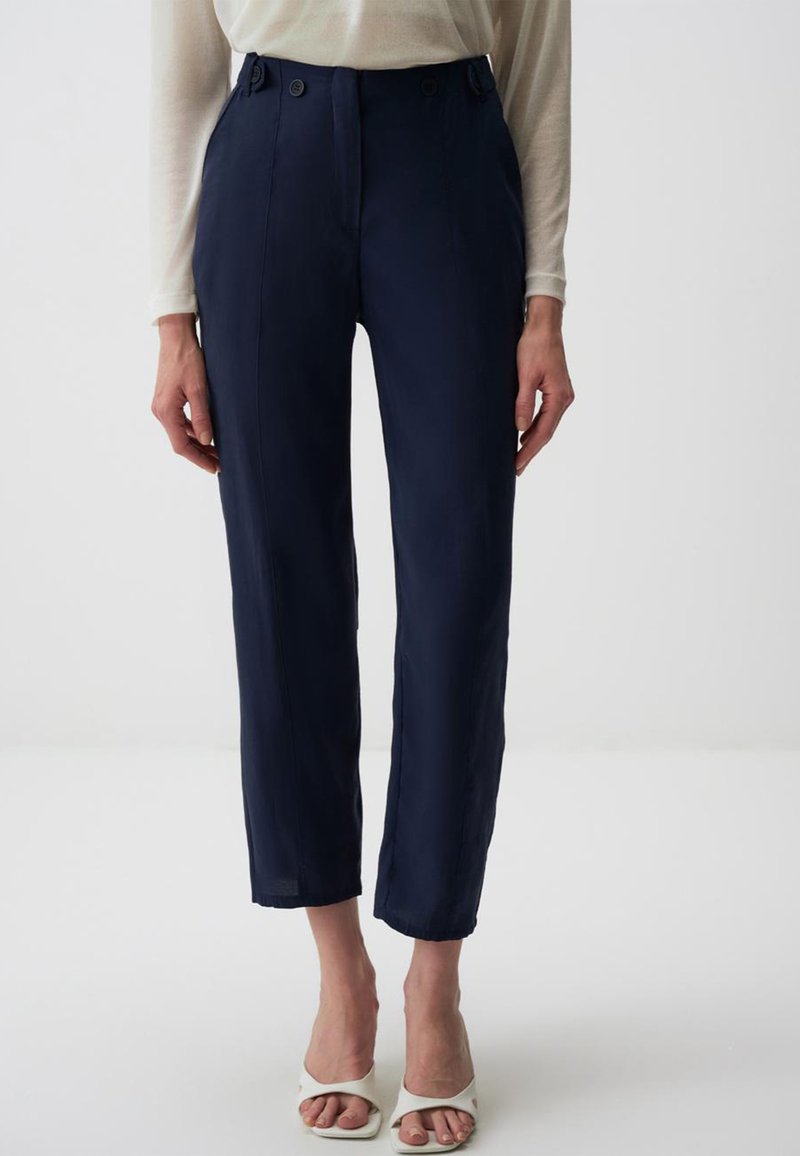 Marineblaue, schlank geschnittene Hose mit hoher Taille, ausgestattet mit zwei vorderen Knöpfen und einem cropped Design, kombiniert mit weißen offenen Schuhen.