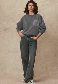Grijze sweatshirt met een voorzak, gecombineerd met hooggecontourde, wijde donkerdenim jeans. De stof lijkt zacht en heeft een casual pasvorm.