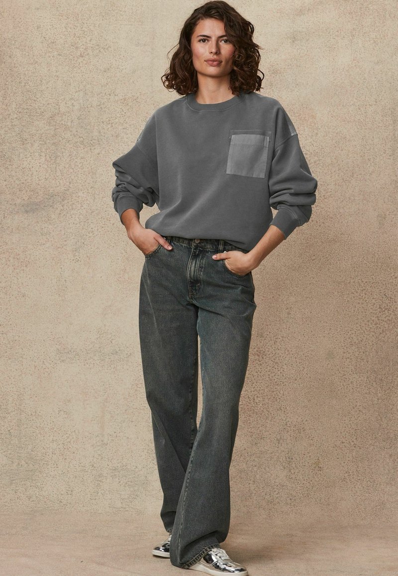 Grijze sweatshirt met een voorzak, gecombineerd met hooggecontourde, wijde donkerdenim jeans. De stof lijkt zacht en heeft een casual pasvorm.