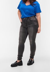 Jeans ajustados negros con un diseño desgastado, bolsillos frontales y cintura alta, combinados con una camiseta azul de escote en V y mocasines negros de plataforma.