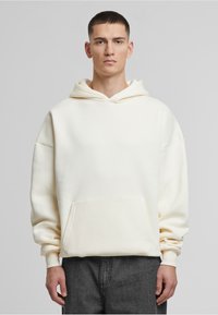 Weißes Kapuzensweatshirt mit Kängurutasche, mit fallenden Schultern und gerippten Bündchen. Glatte Textur, lockerer Schnitt.