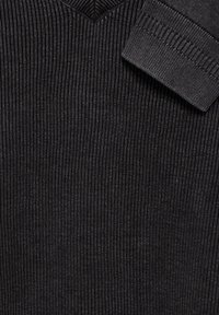 Svart ribbad stickad tröja med V-Hals och vikta ärmslut, tillverkad av ett strukturerat tyg för ökad djup och detalj.