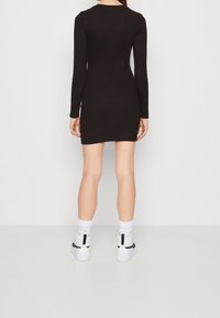 Black long-sleeve dress with a fitted silhouette, pair of white high-top sneakers, and contrasting black accents on the shoes.