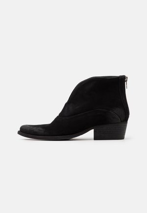 Bottine noire en daim avec petit talon bloc et fermeture éclair à l’arrière, profil latéral sur fond blanc.