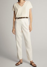 Kermainen v-kauluksinen toppi, rento malli, yhdistetty valkoisiin suoralahkeisiin housuihin. Ruskea vyö korostaa vyötäröä. Mustat tasapohjaiset sandaalit viimeistelevät asun.