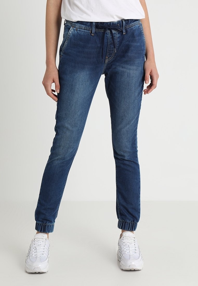 Pantalones jogger de mezclilla azul con puños elásticos y cintura ajustable con cordón. Presentan un diseño clásico de cinco bolsillos y un sutil desgaste en la tela.