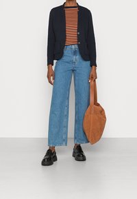 Blazer navy, top a rayas naranja y navy, vaqueros de pierna ancha en azul claro, zapatos de plataforma negros y bolso de ante marrón con correa para el hombro.