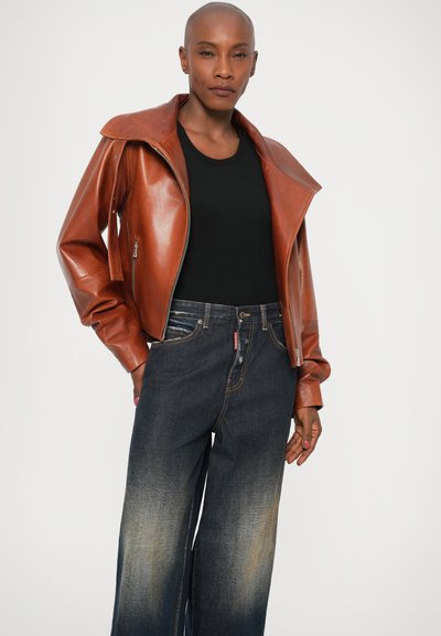 Chaqueta de cuero marrón con un cuello ancho, con la parte delantera sin abrochar, combinada con jeans de pierna ancha de color azul oscuro que presentan un ligero desvanecimiento y detalles en los bolsillos.