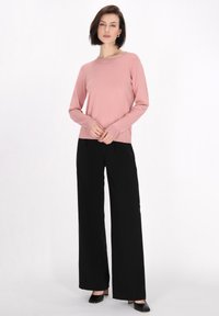 Világos rózsaszín, hosszú ujjú pulóver, kerek nyakkivágással, fekete, széles lábú nadrággal és fekete, hegyes orrú magassarkú cipővel párosítva, sima textúrával.