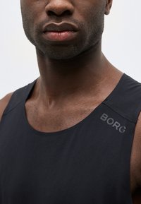 Κοντινό πλάνο ενός άνδρα που φοράει μαύρο αμάνικο αθλητικό τοπ με την επιγραφή "BORG" στον αριστερό ώμο.