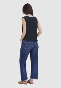 Dunkelblaues, geripptes, ärmelloses Oberteil, kombiniert mit hellblauen, geraden Jeans mit dezentem Used-Look und Gesäßtaschen. Breite Sandalen rundet das Outfit ab.