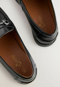 Sorte læder loafers med et strømlinet design, der har en sølvmetal detalje og brune læderindlæg. Glat tekstur og afrundet form.