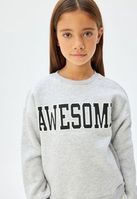 Szara bluzka z miękkiego materiału z wyrazem "AWESOME" w wyraźnym czarnym druku na przodzie. Okrągły dekolt i luźny krój.