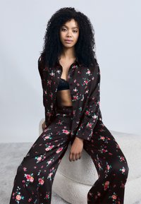 Ensemble de pyjama noir à motifs floraux avec de petites roses rouges et turquoise, comprenant une chemise ample à boutons et un pantalon à jambes larges avec une finition textile douce.