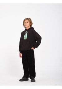 Zwarte hoodie met een grafisch ontwerp met een UFO en een groen stekelig element, gecombineerd met zwarte corduroy broeken en zwarte sneakers.
