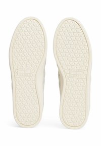 Suelas de zapatos de color crema con un patrón texturizado de diamante. Presenta una marca en relieve y un borde suave y goma.
