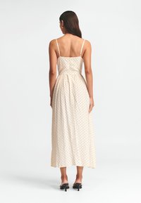 Beige Maxikleid mit Pünktchen, dünnen Trägern, tailliertem Oberteil und gerafftem Bund; fließender Rock mit glatter Textur.