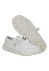 Zapatillas de lona blancas con un upper texturizado, puntera redonda, un cordón mínimo y una suela de goma con un patrón de estrellas y un logotipo en relieve.