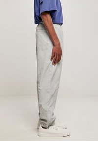 Lysegrå, letvægtsbukser med elastik i talje og manchetter. Bruges sammen med en lilla kortærmet skjorte og hvide sneakers, vist i profil.