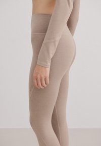Beige high-waisted leggings gemaakt van naadloze, rekbare stof, met een subtiel logo op de dij en een gladde, strakke textuur.