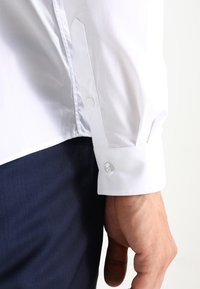 Witte overhemdmanchet met een knoop, met een gladde textuur en gestructureerd ontwerp. In combinatie met marineblauwe broek.