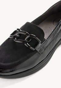 Mocassin noir à enfiler avec dessus en daim, côtés en cuir brillant et un grand détail chaîne métallique noire à l'avant.