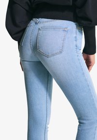 Svijetloplave skinny traperice s glatkom teksturom, koje imaju stražnje džepove i detaljno šivanje duž šavova.