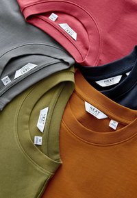 Four T-shirts in gray, pink, olive green, and burnt orange, featuring crew necklines and labels indicating size and brand.