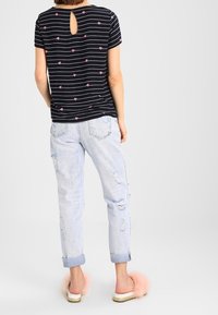 T-shirt rayé noir avec des cœurs roses, détail dos en forme de trou de serrure. Porté avec un jean bleu clair déchiré et des sandales roses en peluche.