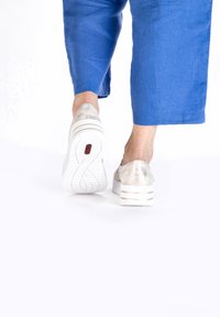Silver slip-on shoes with a textured upper, white platform sole featuring two stripes, paired with blue cropped pants.