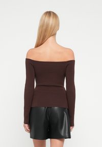 Σκούρο καφέ πουλόβερ με σκέτες τις ώμους και μακριά μανίκια, με ραβδωτή υφή, εφαρμοστή σχεδίαση και ελαφρώς φαρδιά τελειώματα στο κάτω μέρος, συνδυασμένο με μαύρο δερμάτινο σορτς.