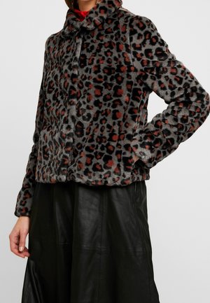 Woman wearing a grey and brown leopard print faux fur jacket with a red collar detail and black leather skirt, hand in pocket.