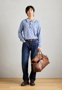 Chemise en tricot à motif bleu clair avec col et boutons, associée à un jean bleu foncé, une ceinture en cuir marron et un grand sac en cuir marron.