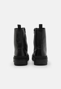 Botas de tobillo de cuero negro con un diseño elegante, cremalleras laterales y una suela de goma gruesa. Parte trasera texturizada y tiradores en bucle para poner y quitar fácilmente.