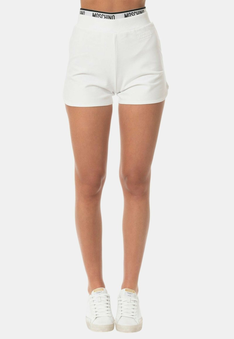 Pantaloni corti bianchi con un design semplice, fascia elastica in vita con testo del logo nero e una texture liscia. Abbinati a sneakers bianche.