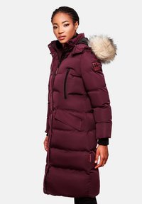Burgundy puffer coat with a fur-lined hood, zippered pockets, and elastic cuffs. Features a quilted design and a logo detail on the sleeve.