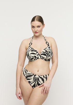 Vrouw met strak naar achteren gekamd haar, gekleed in een zwart-witte bikini met zebraprint, poseert tegen een effen witte achtergrond.