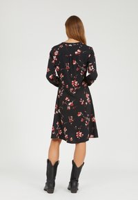 Vestido negro con estampado floral, de mangas largas, que presenta un patrón de flores en rojo y blanco. Tiene un corte holgado con un dobladillo a la altura de la rodilla. Combinado con botas negras.