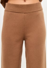 Pantaloni tricotati maro cu un brâu elastic cu nervuri, având o textură netedă și un design cu picioare drepte.