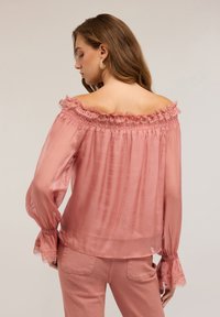Blusa rosa off-the-shoulder in tessuto trasparente con finiture in pizzo al collo e ai polsini; presenta maniche lunghe e fluenti e un fit rilassato.