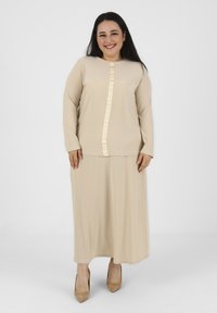 Abito beige a maniche lunghe con taglio dritto, caratterizzato da un nastro verticale lungo la parte frontale e una texture di tessuto liscia e morbida.