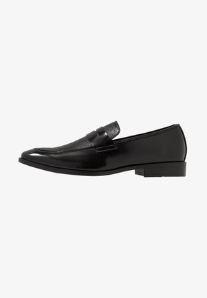 Mocassin homme en cuir noir avec un petit talon, un bout arrondi et un détail de bride sur le dessus, vu de profil sur fond blanc.